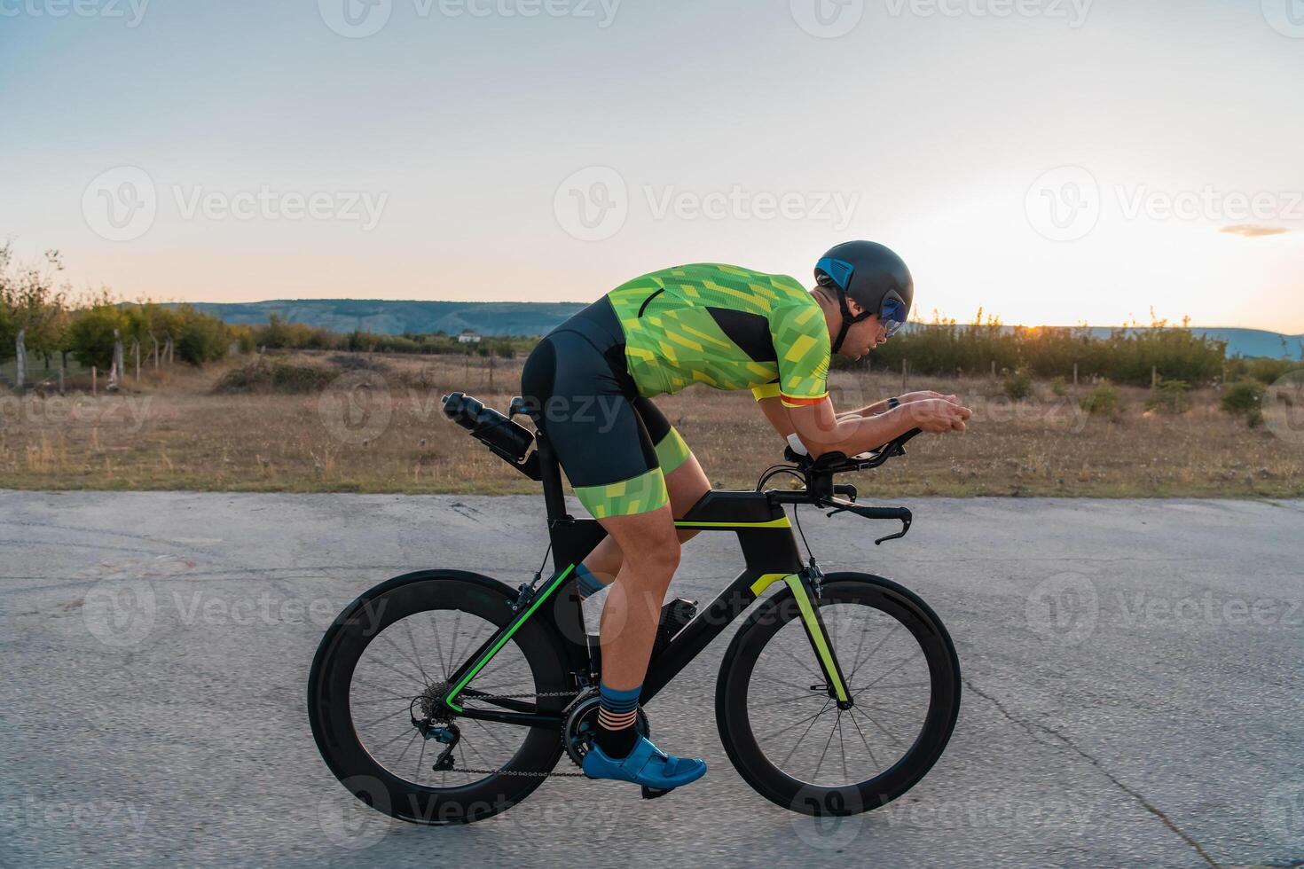 Triathlete riding his bicycle during sunset, preparing for a marathon. The warm colors of the sky provide a beautiful backdrop for his determined and focused effort. photo