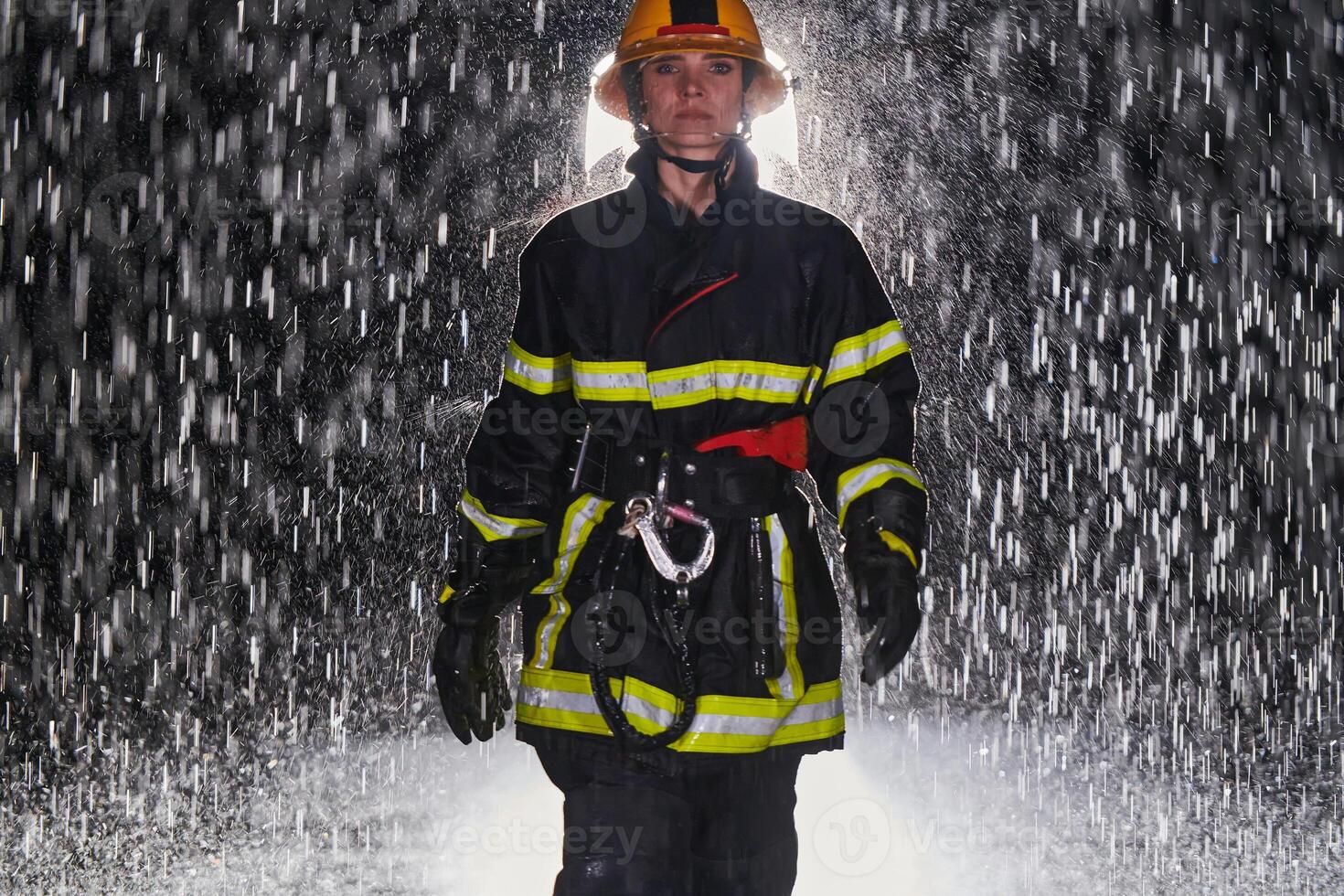 A determined female firefighter in a professional uniform striding through the dangerous, rainy night on a daring rescue mission, showcasing her unwavering bravery and commitment to saving lives. photo