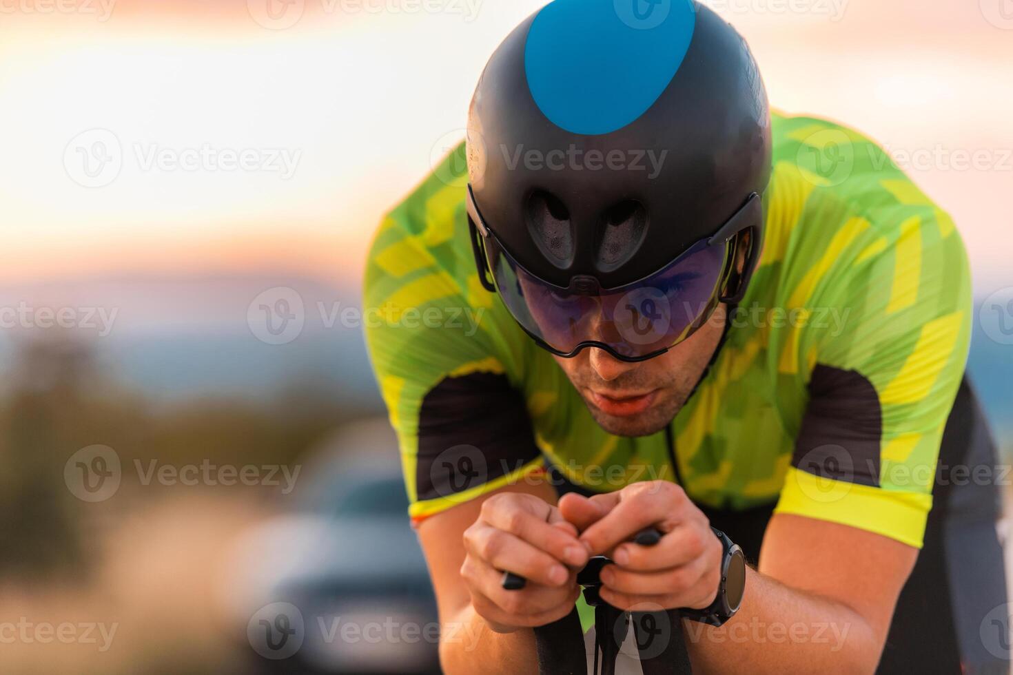 Close up photo of triathlete riding his bicycle during sunset, preparing for a marathon. The warm colors of the sky provide a beautiful backdrop for his determined and focused effort.