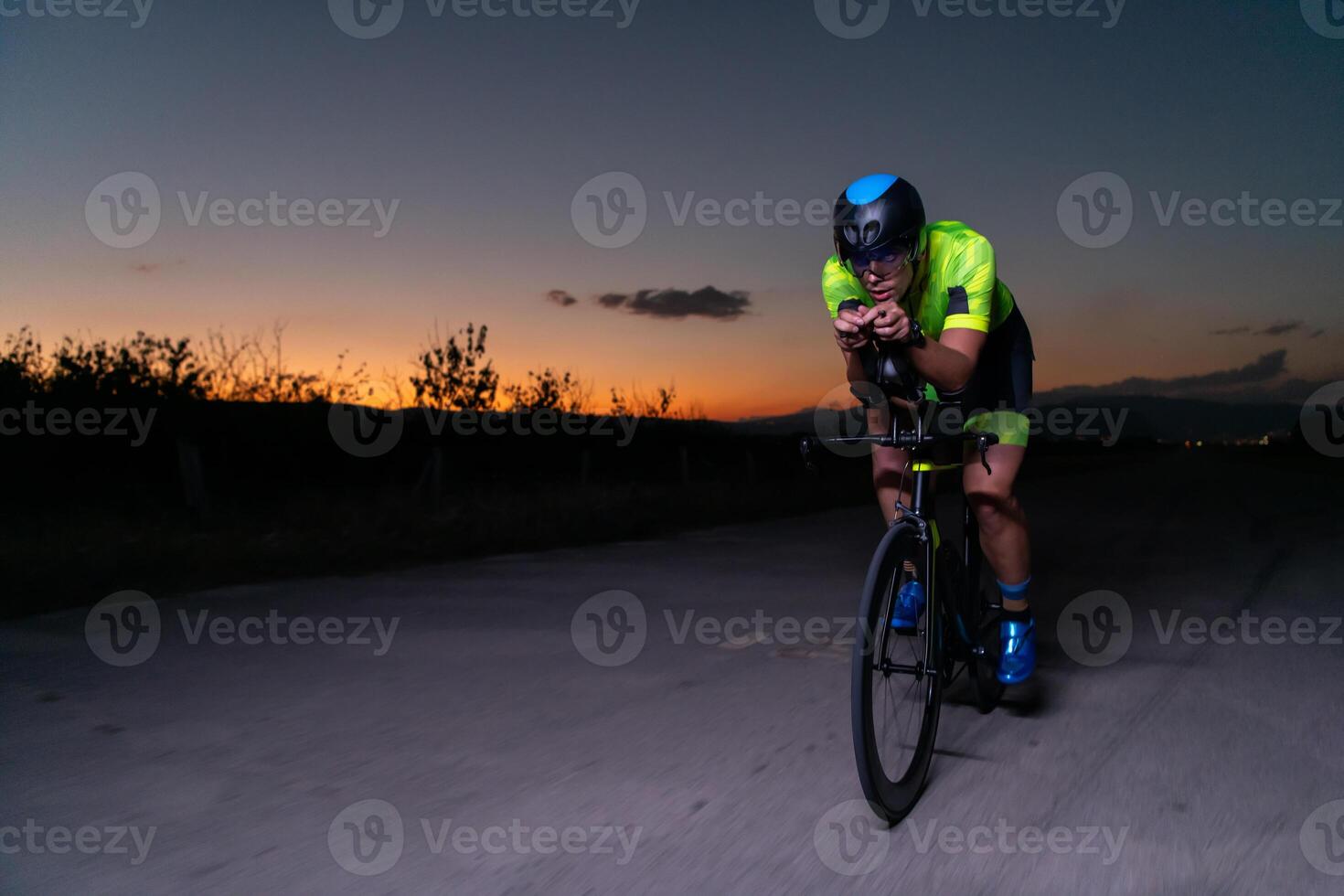 A triathlete rides his bike in the darkness of night, pushing himself to prepare for a marathon. The contrast between the darkness and the light of his bike creates a sense of drama and highlights the photo