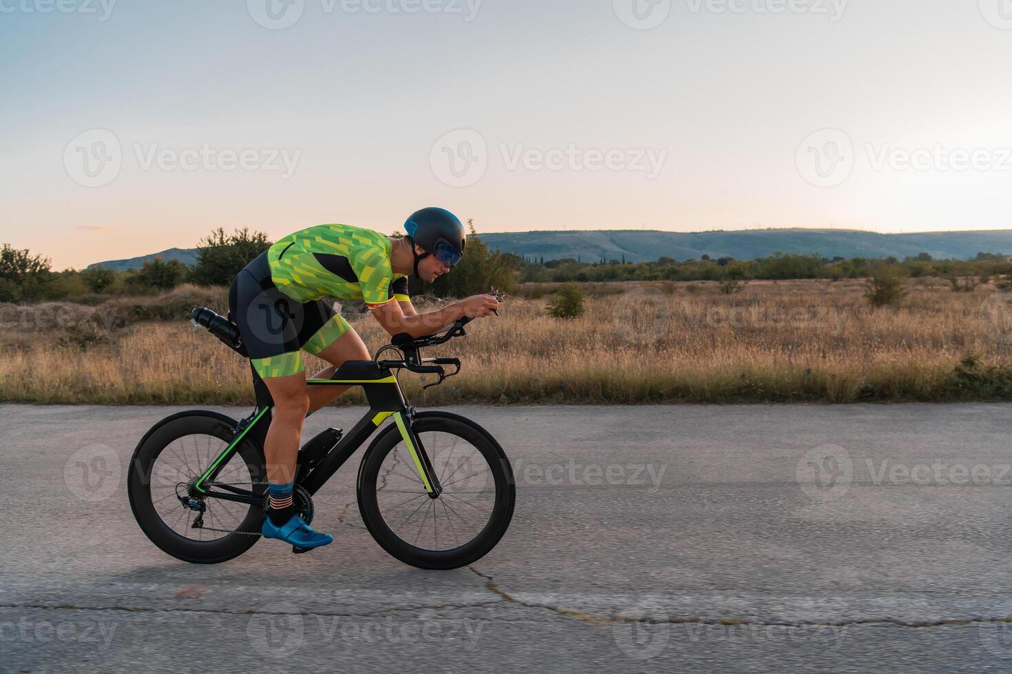 Triathlete riding his bicycle during sunset, preparing for a marathon. The warm colors of the sky provide a beautiful backdrop for his determined and focused effort. photo
