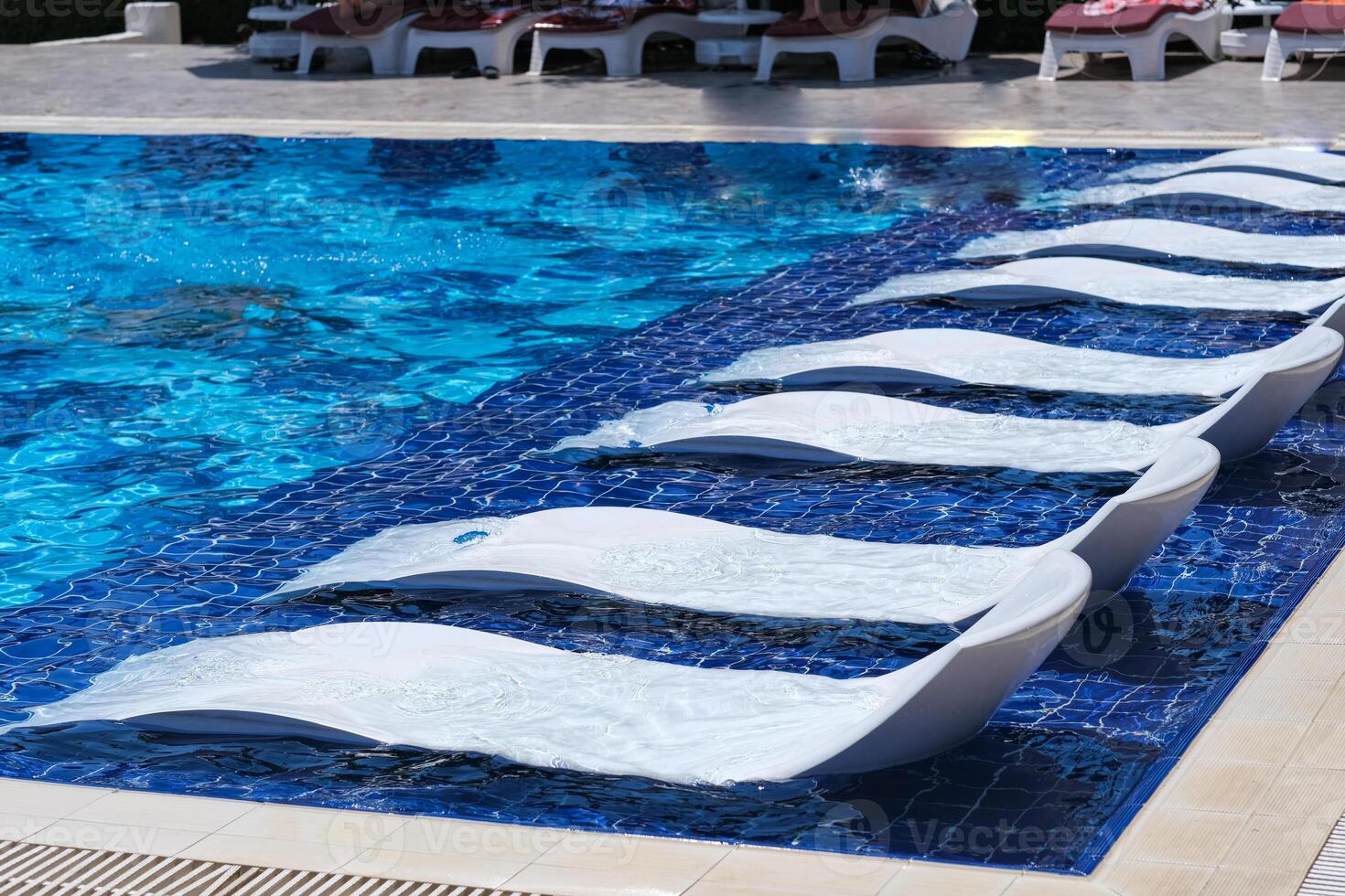 A pool with a row of white lounge chairs on the side photo