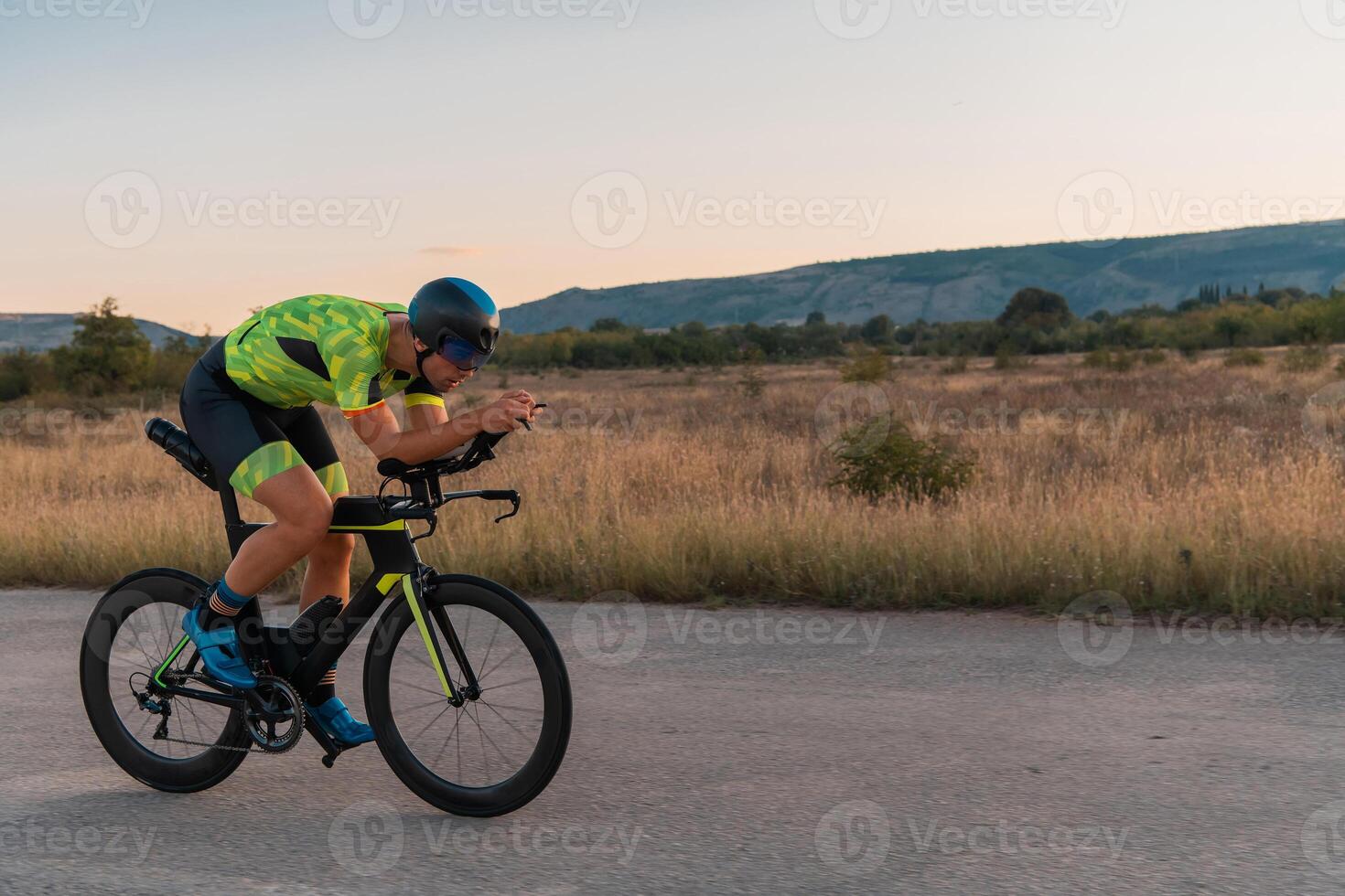 Triathlete riding his bicycle during sunset, preparing for a marathon. The warm colors of the sky provide a beautiful backdrop for his determined and focused effort. photo