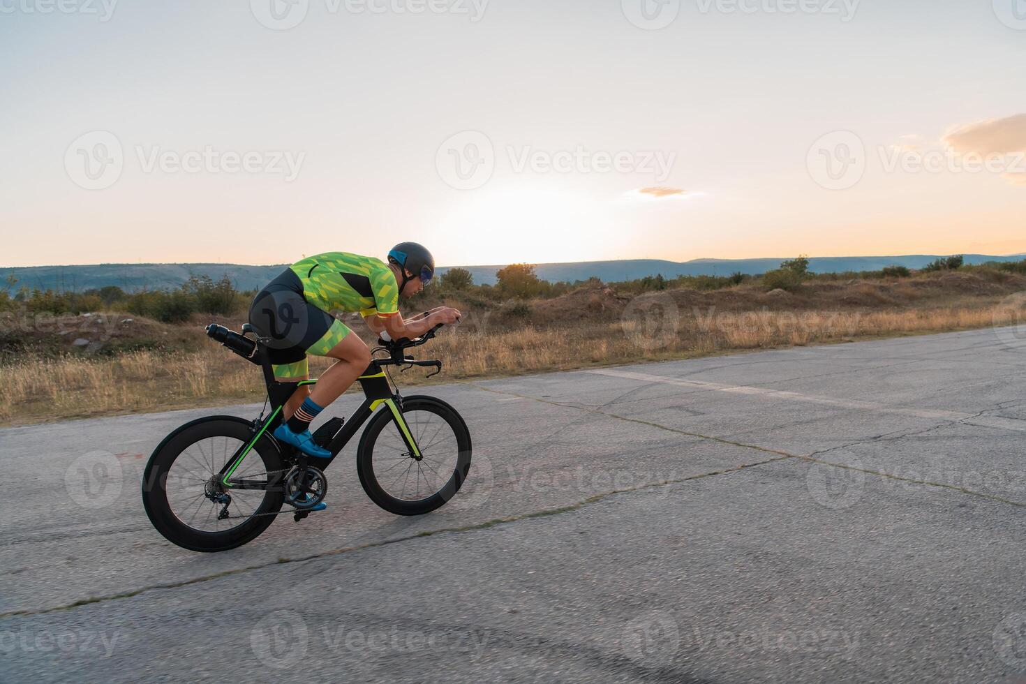 Triathlete riding his bicycle during sunset, preparing for a marathon. The warm colors of the sky provide a beautiful backdrop for his determined and focused effort. photo