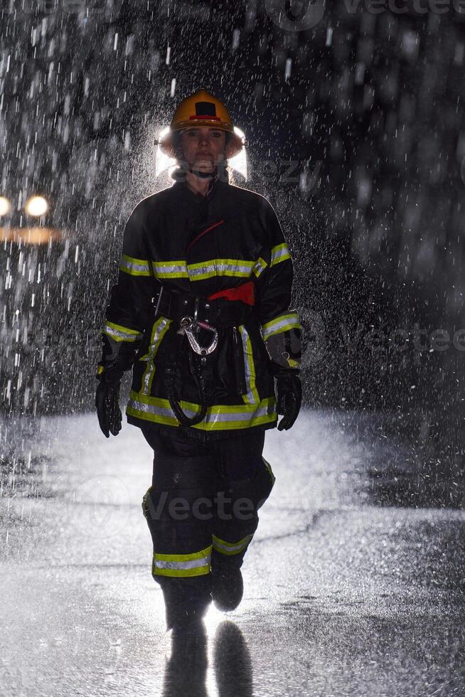 A determined female firefighter in a professional uniform striding through the dangerous, rainy night on a daring rescue mission, showcasing her unwavering bravery and commitment to saving lives. photo