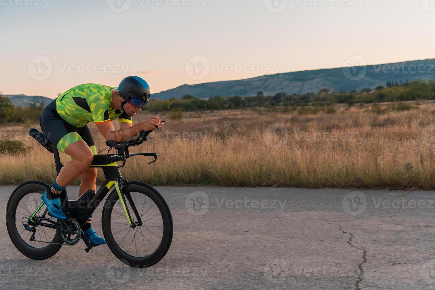 Triathlete riding his bicycle during sunset, preparing for a marathon. The warm colors of the sky provide a beautiful backdrop for his determined and focused effort. photo