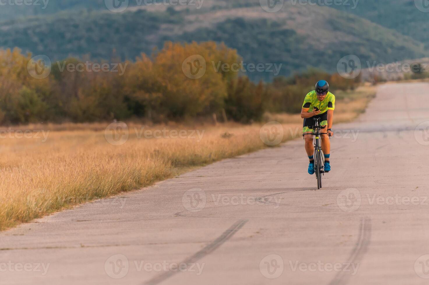 Triathlete riding his bicycle during sunset, preparing for a marathon. The warm colors of the sky provide a beautiful backdrop for his determined and focused effort. photo
