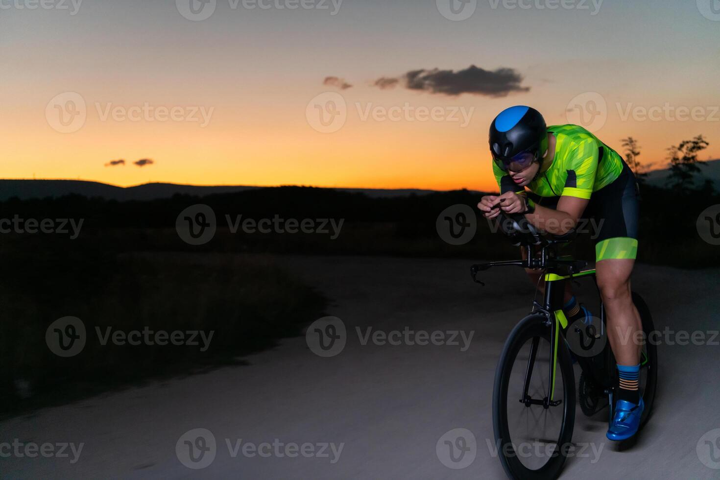 A triathlete rides his bike in the darkness of night, pushing himself to prepare for a marathon. The contrast between the darkness and the light of his bike creates a sense of drama and highlights the photo