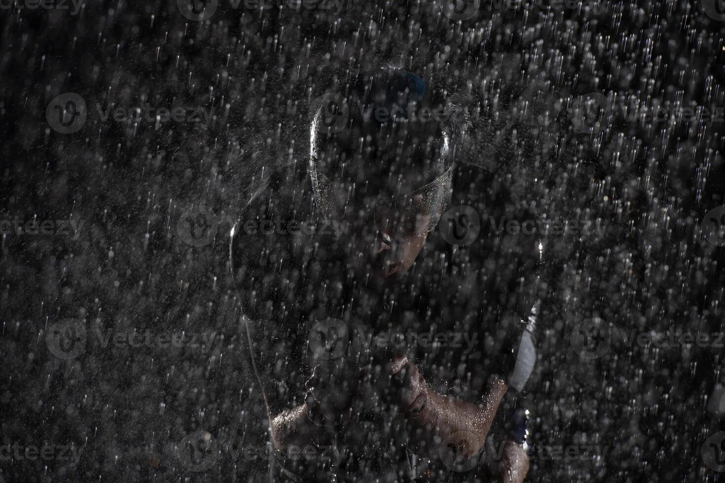 A triathlete braving the rain as he cycles through the night, preparing himself for the upcoming marathon. The blurred raindrops in the foreground and the dark, moody atmosphere in the background add photo