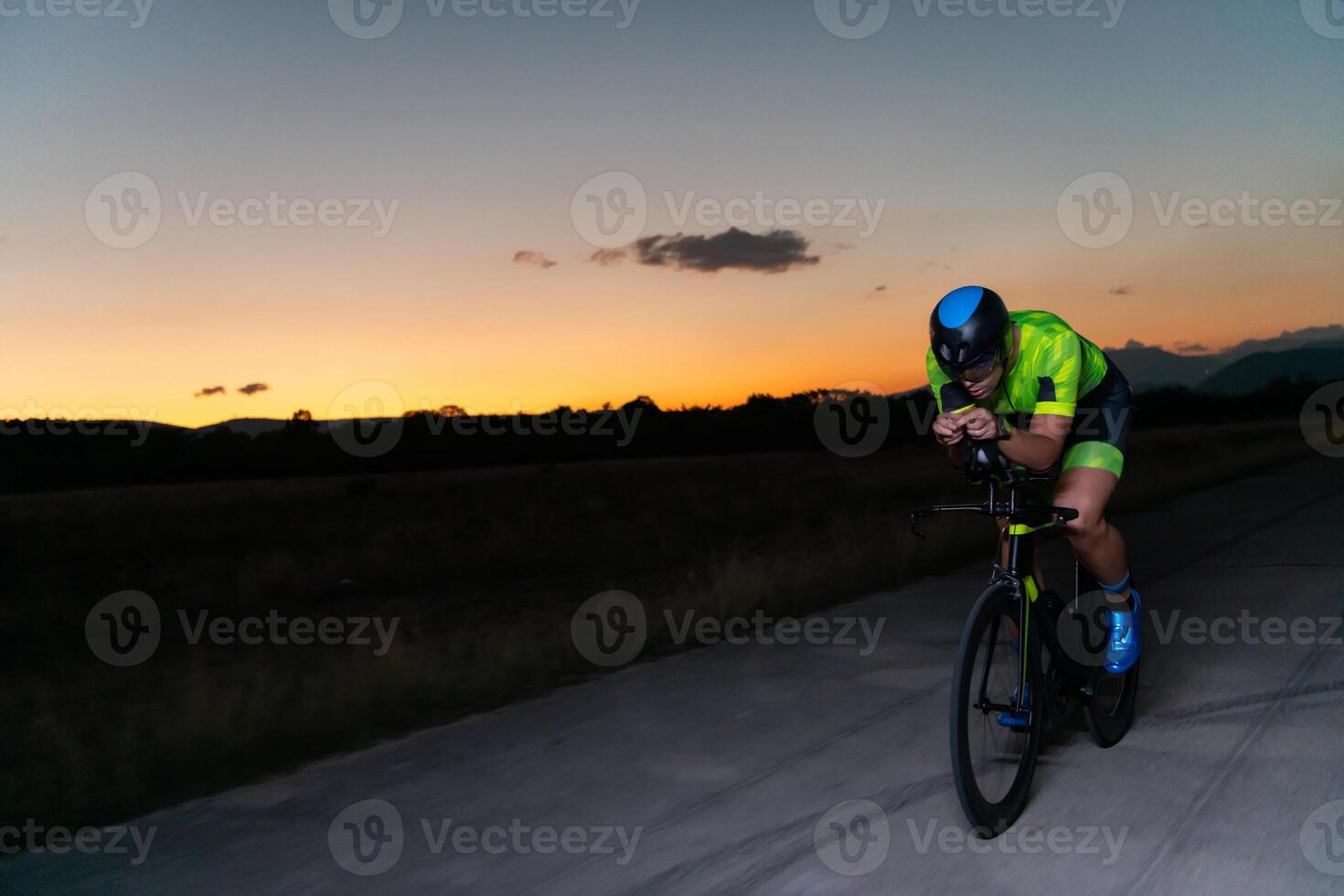 A triathlete rides his bike in the darkness of night, pushing himself to prepare for a marathon. The contrast between the darkness and the light of his bike creates a sense of drama and highlights the photo