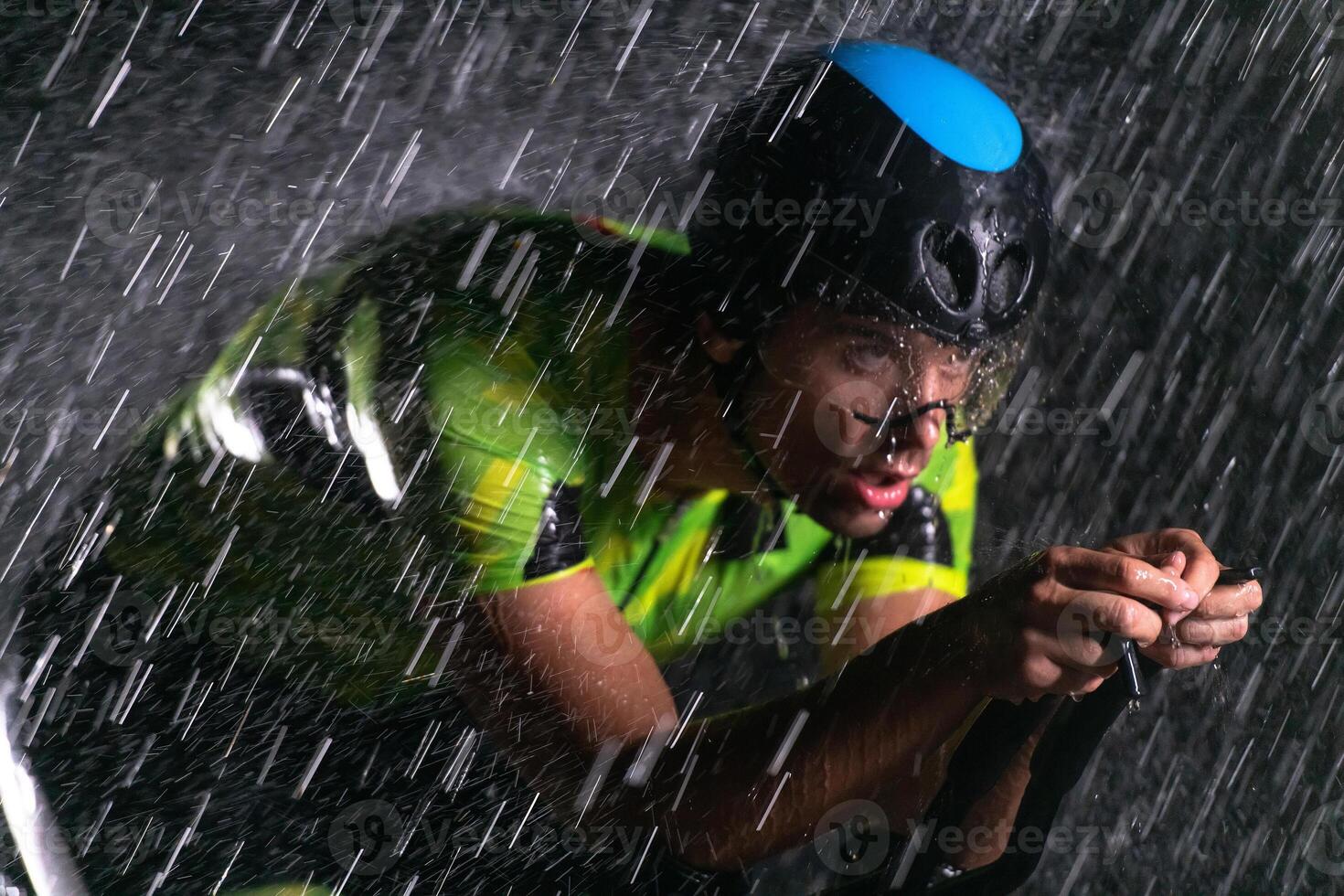 A triathlete braving the rain as he cycles through the night, preparing himself for the upcoming marathon. The blurred raindrops in the foreground and the dark, moody atmosphere in the background add photo