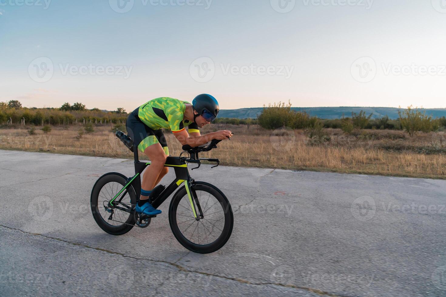Triathlete riding his bicycle during sunset, preparing for a marathon. The warm colors of the sky provide a beautiful backdrop for his determined and focused effort. photo