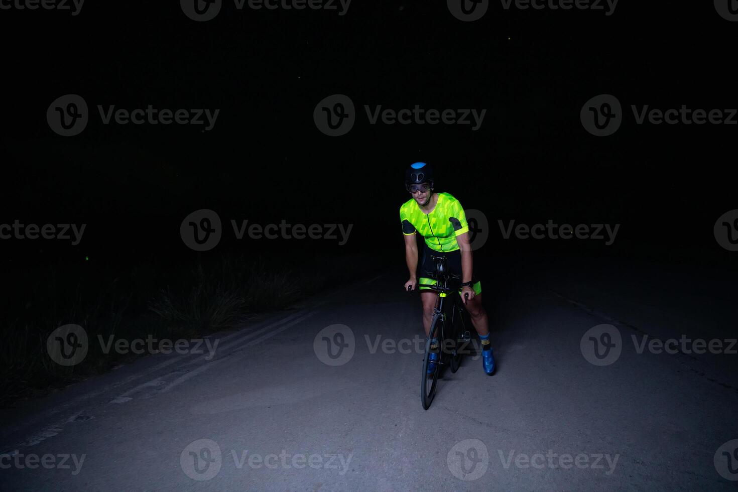 A triathlete rides his bike in the darkness of night, pushing himself to prepare for a marathon. The contrast between the darkness and the light of his bike creates a sense of drama and highlights the photo