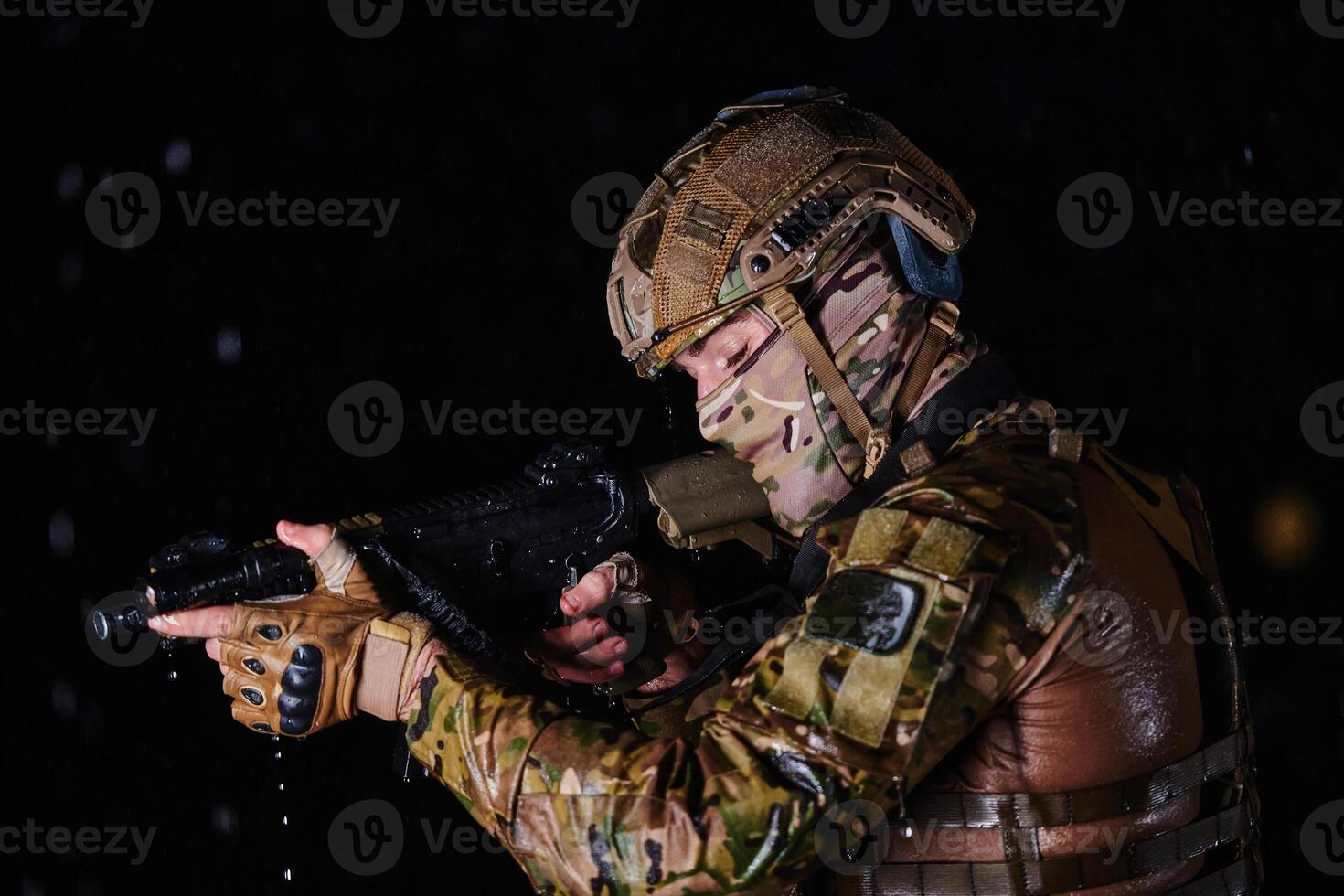 Army soldier in Combat Uniforms with an assault rifle, plate carrier and combat helmet going on a dangerous mission on a rainy night. photo
