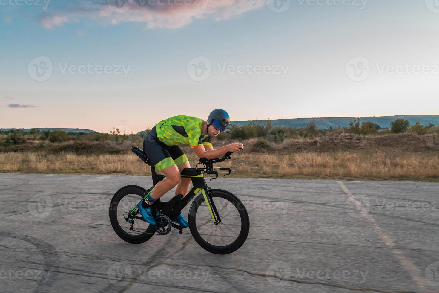 Triathlete riding his bicycle during sunset, preparing for a marathon. The warm colors of the sky provide a beautiful backdrop for his determined and focused effort. photo
