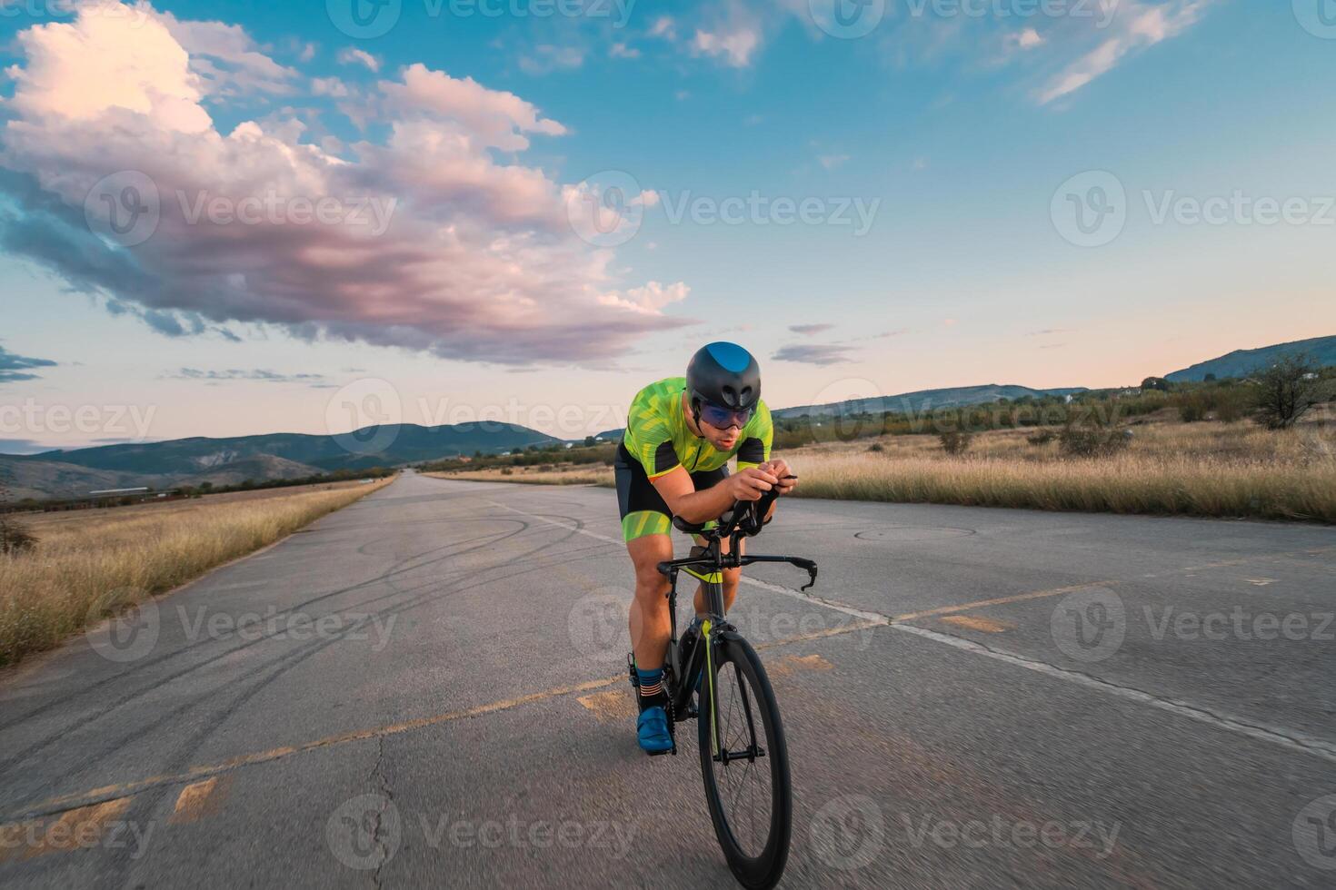 Triathlete riding his bicycle during sunset, preparing for a marathon. The warm colors of the sky provide a beautiful backdrop for his determined and focused effort. photo