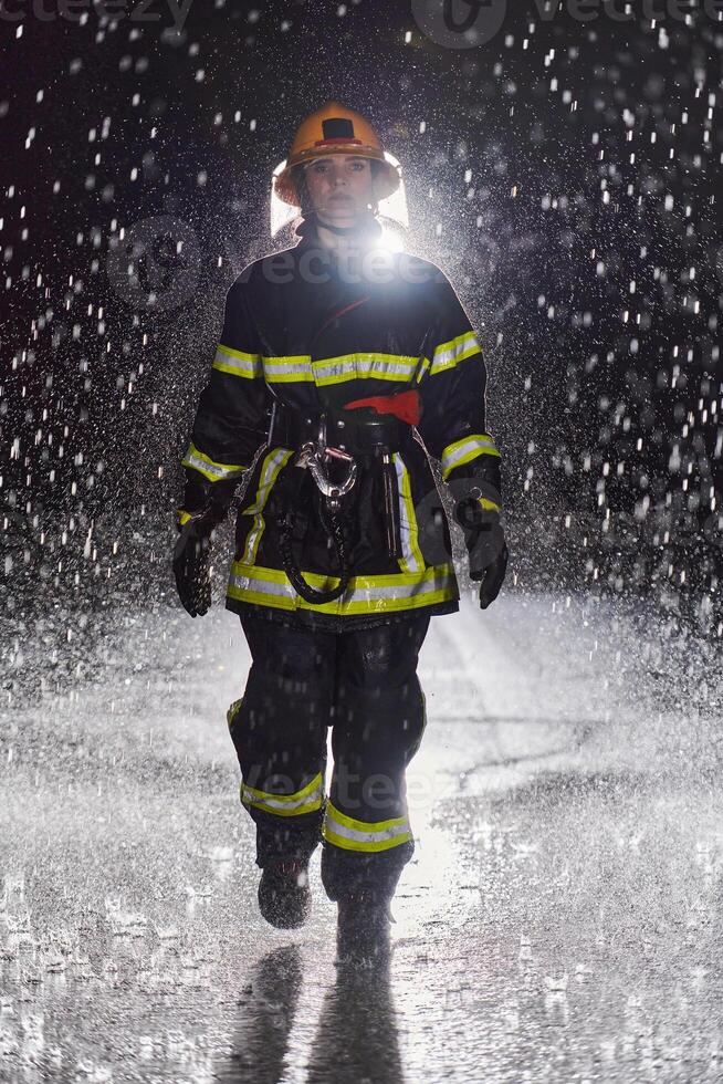 A determined female firefighter in a professional uniform striding through the dangerous, rainy night on a daring rescue mission, showcasing her unwavering bravery and commitment to saving lives. photo
