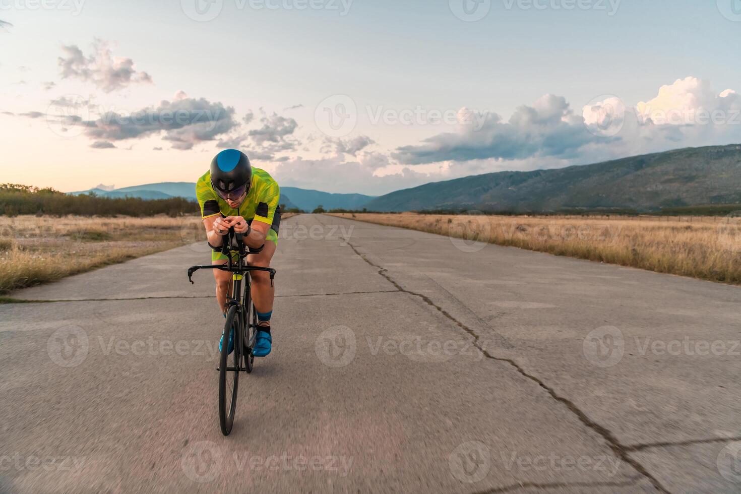 Triathlete riding his bicycle during sunset, preparing for a marathon. The warm colors of the sky provide a beautiful backdrop for his determined and focused effort. photo