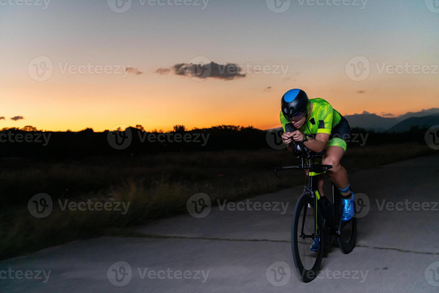 A triathlete rides his bike in the darkness of night, pushing himself to prepare for a marathon. The contrast between the darkness and the light of his bike creates a sense of drama and highlights the photo