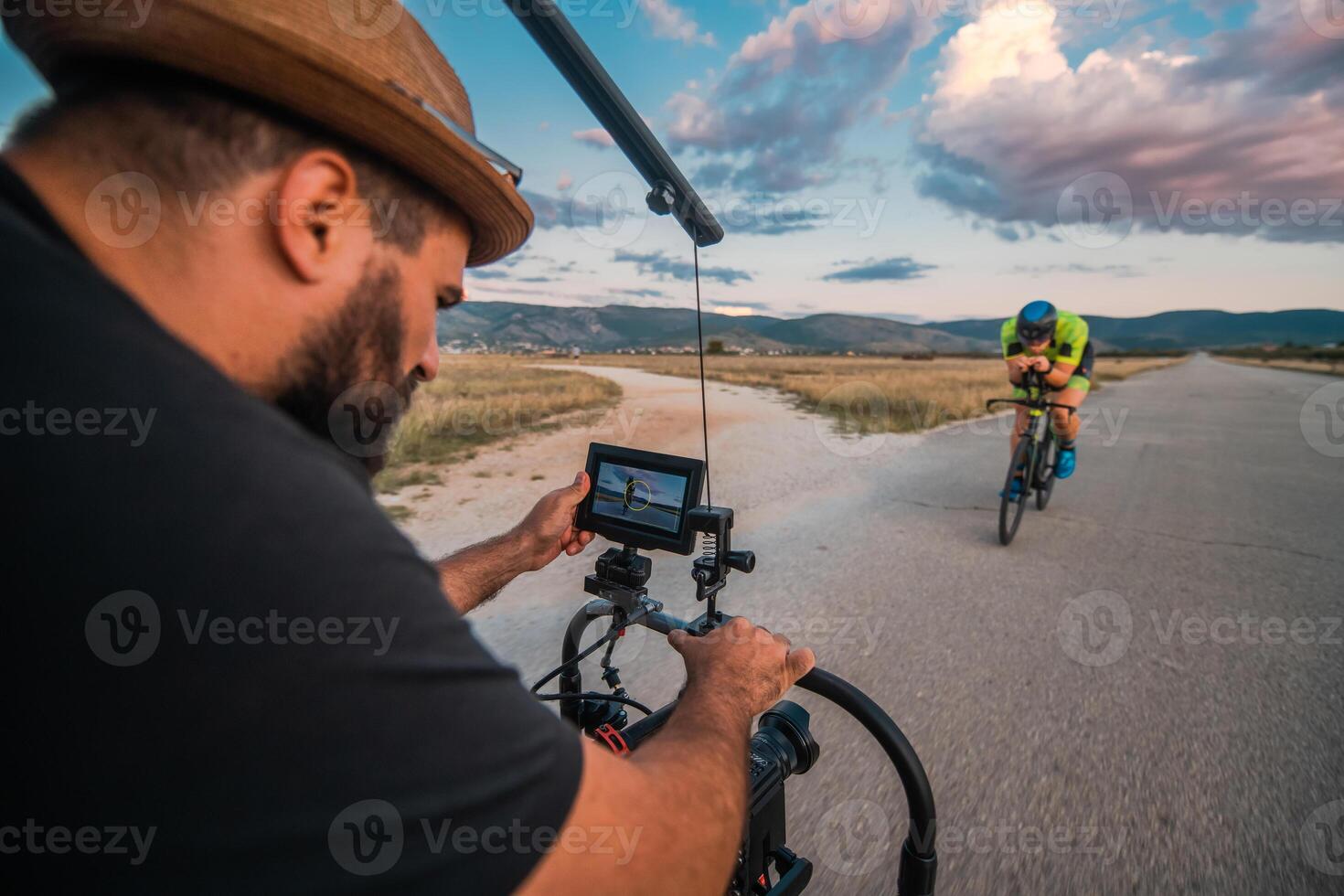 A videographer recording a triathlete riding his bike preparing for an upcoming marathon.Athlete's physical endurance and the dedication required to succeed in the sport. photo