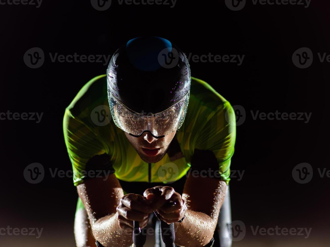 A triathlete rides his bike in the darkness of night, pushing himself to prepare for a marathon. The contrast between the darkness and the light of his bike creates a sense of drama and highlights the photo