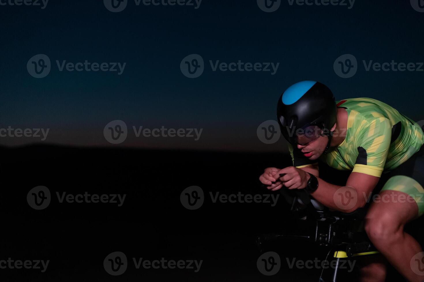 A triathlete rides his bike in the darkness of night, pushing himself to prepare for a marathon. The contrast between the darkness and the light of his bike creates a sense of drama and highlights the photo