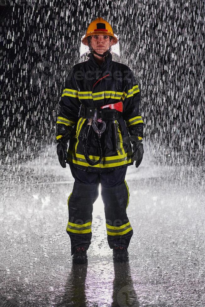 A determined female firefighter in a professional uniform striding through the dangerous, rainy night on a daring rescue mission, showcasing her unwavering bravery and commitment to saving lives. photo