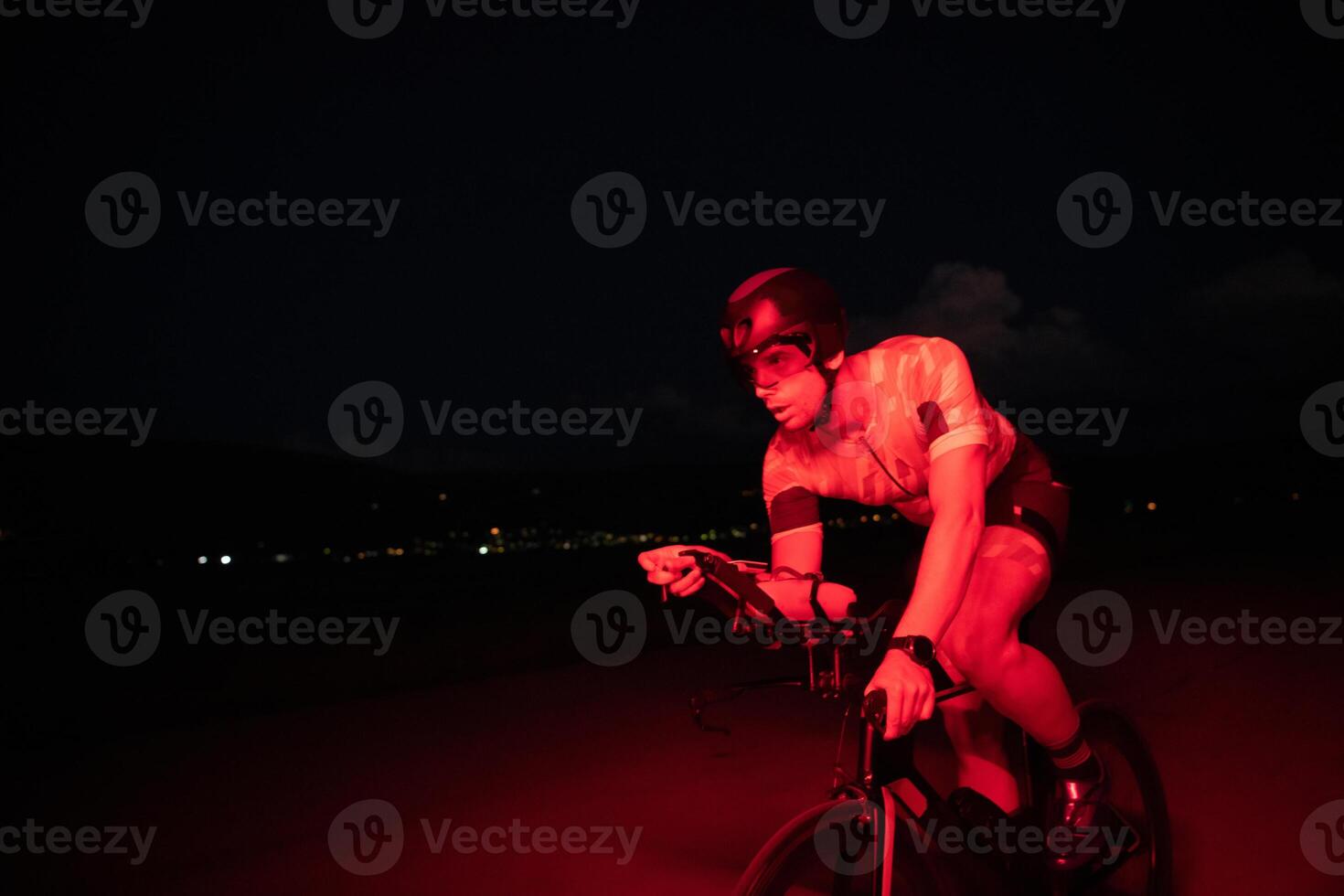 A triathlete rides his bike in the darkness of night, pushing himself to prepare for a marathon. The contrast between the darkness and the light of his bike creates a sense of drama and highlights the photo