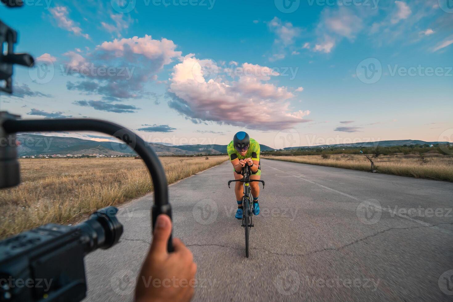 A videographer recording a triathlete riding his bike preparing for an upcoming marathon.Athlete's physical endurance and the dedication required to succeed in the sport. photo