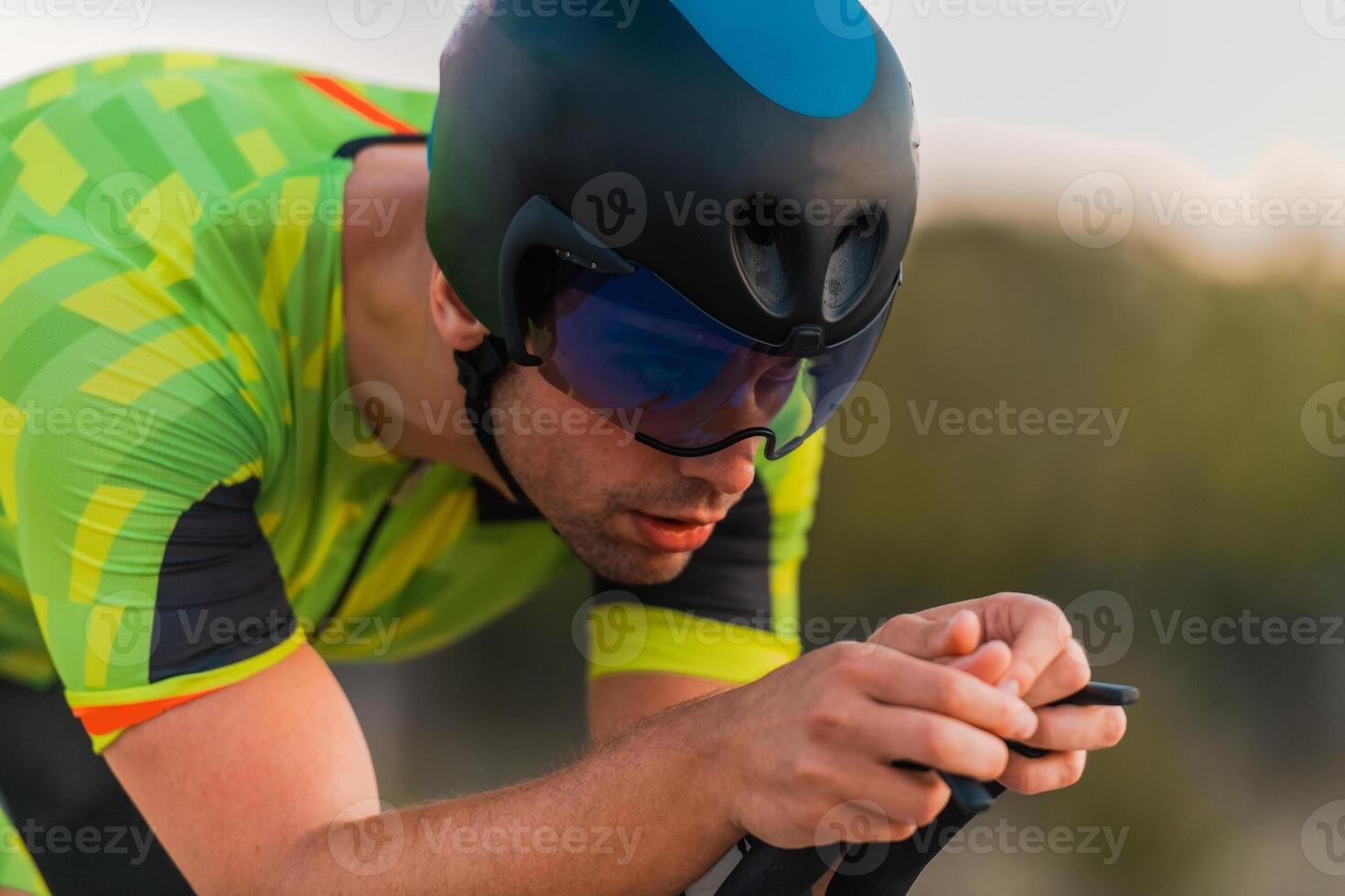 Close up photo of triathlete riding his bicycle during sunset, preparing for a marathon. The warm colors of the sky provide a beautiful backdrop for his determined and focused effort.