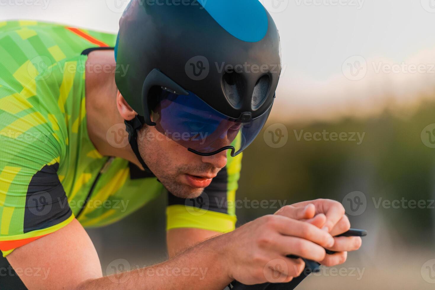 Close up photo of triathlete riding his bicycle during sunset, preparing for a marathon. The warm colors of the sky provide a beautiful backdrop for his determined and focused effort.