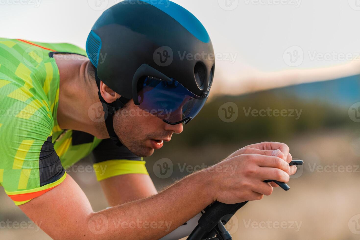 Close up photo of triathlete riding his bicycle during sunset, preparing for a marathon. The warm colors of the sky provide a beautiful backdrop for his determined and focused effort.