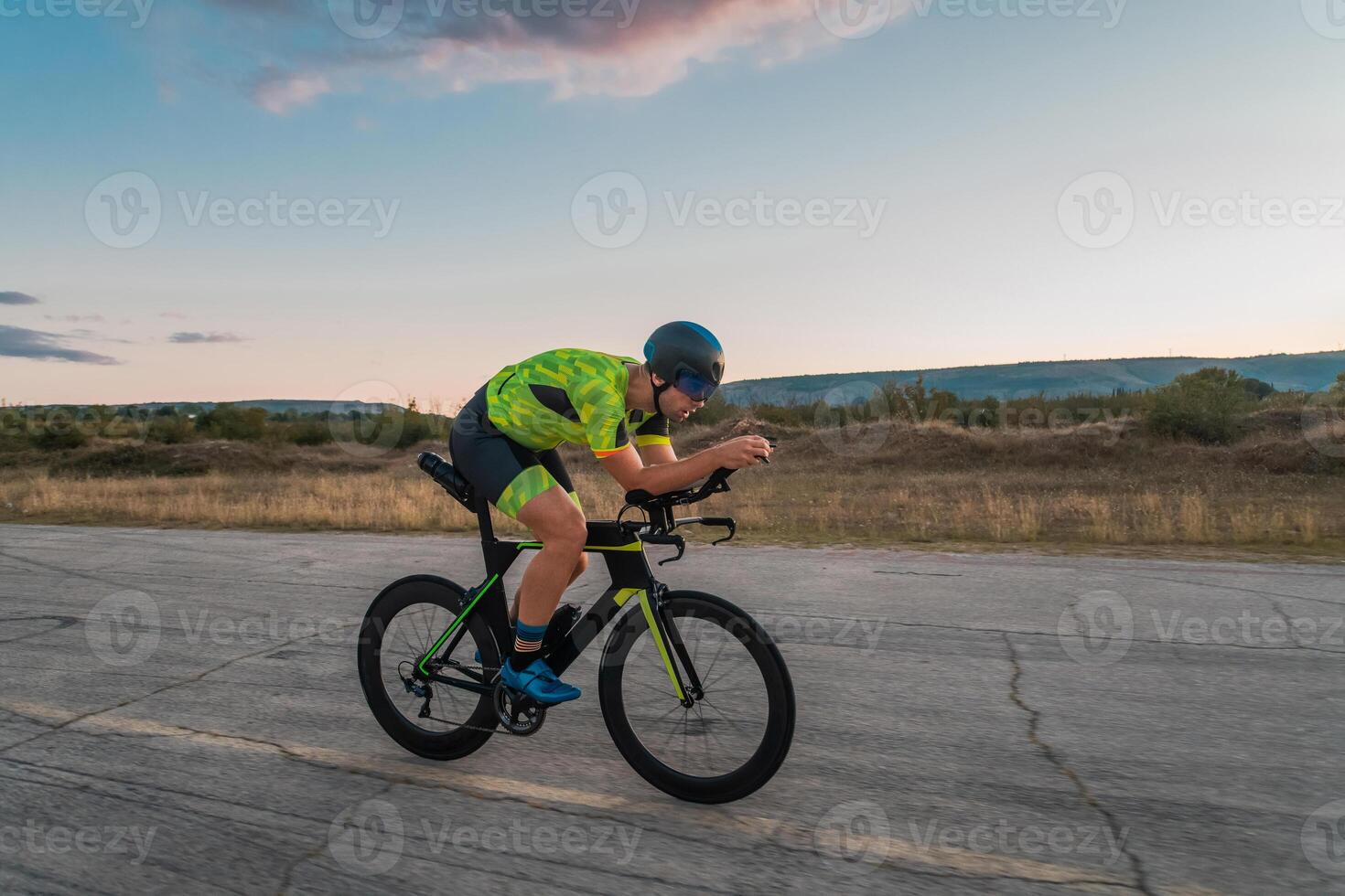 Triathlete riding his bicycle during sunset, preparing for a marathon. The warm colors of the sky provide a beautiful backdrop for his determined and focused effort. photo