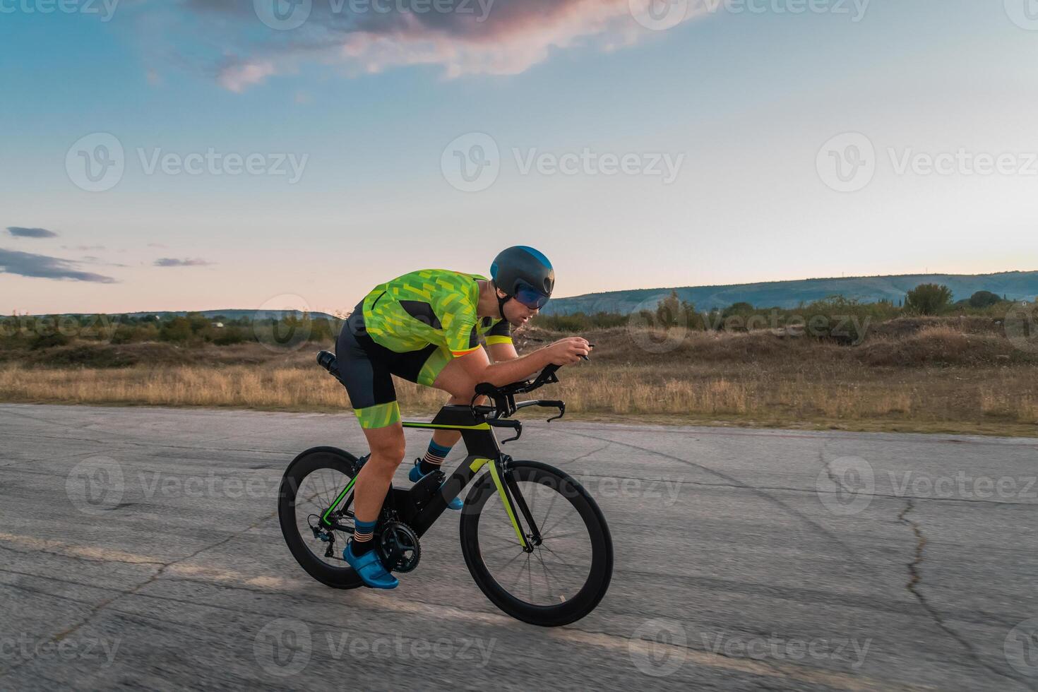 Triathlete riding his bicycle during sunset, preparing for a marathon. The warm colors of the sky provide a beautiful backdrop for his determined and focused effort. photo