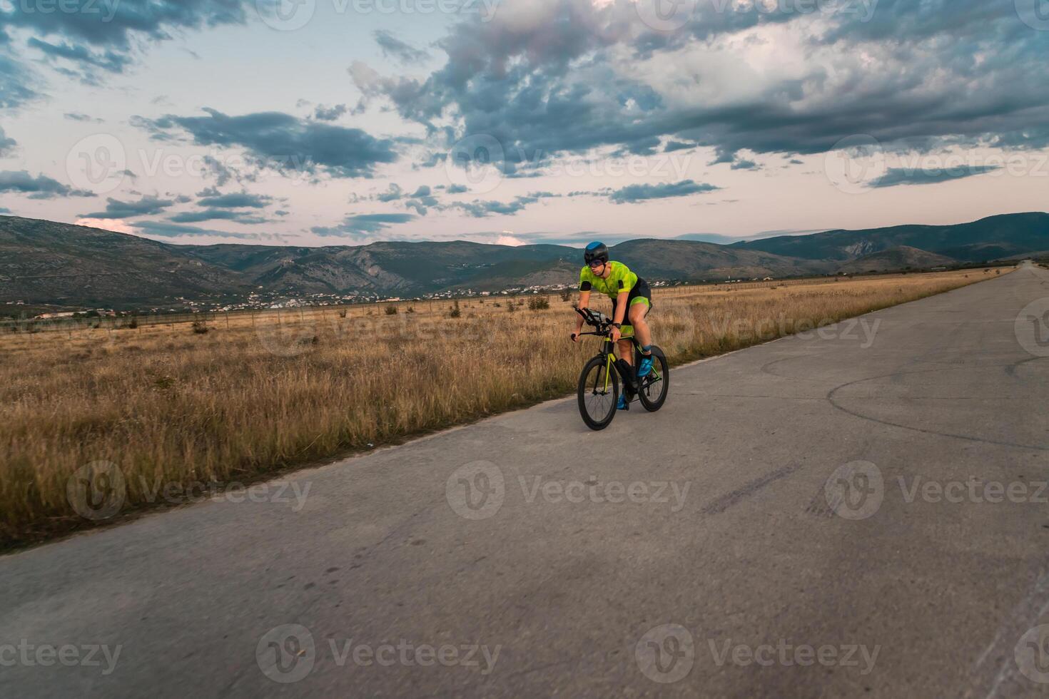 Triathlete riding his bicycle during sunset, preparing for a marathon. The warm colors of the sky provide a beautiful backdrop for his determined and focused effort. photo