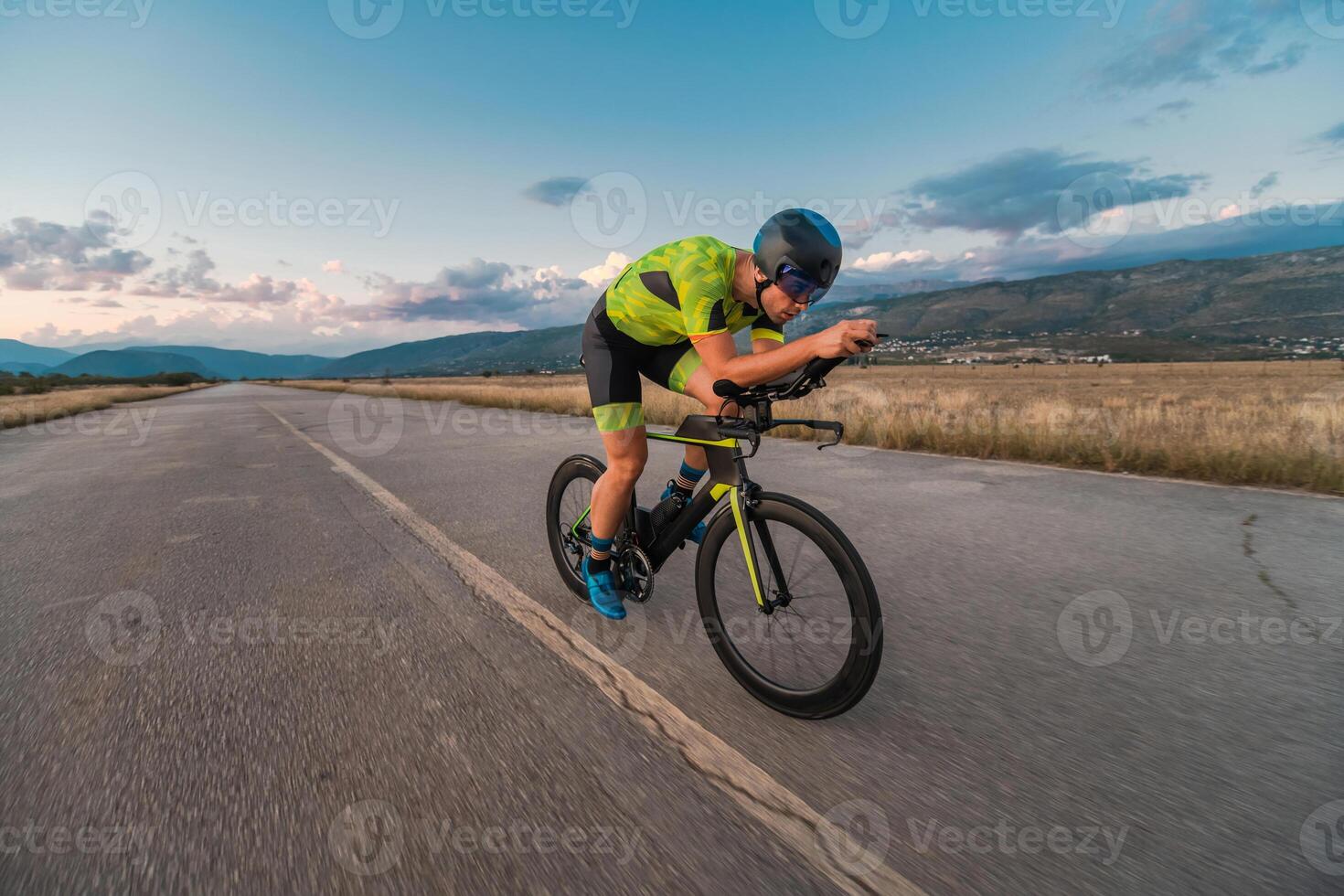 Triathlete riding his bicycle during sunset, preparing for a marathon. The warm colors of the sky provide a beautiful backdrop for his determined and focused effort. photo