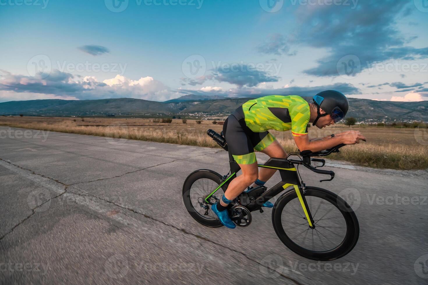 Triathlete riding his bicycle during sunset, preparing for a marathon. The warm colors of the sky provide a beautiful backdrop for his determined and focused effort. photo