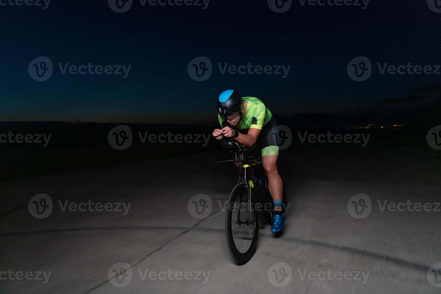 A triathlete rides his bike in the darkness of night, pushing himself to prepare for a marathon. The contrast between the darkness and the light of his bike creates a sense of drama and highlights the photo