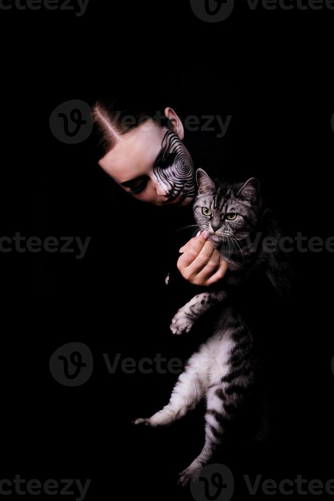 image for Halloween, girl with spiral makeup on her face with a cat in her arms photo