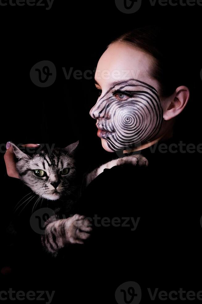 image for Halloween, girl with spiral makeup on her face with a gray cat in her arms photo