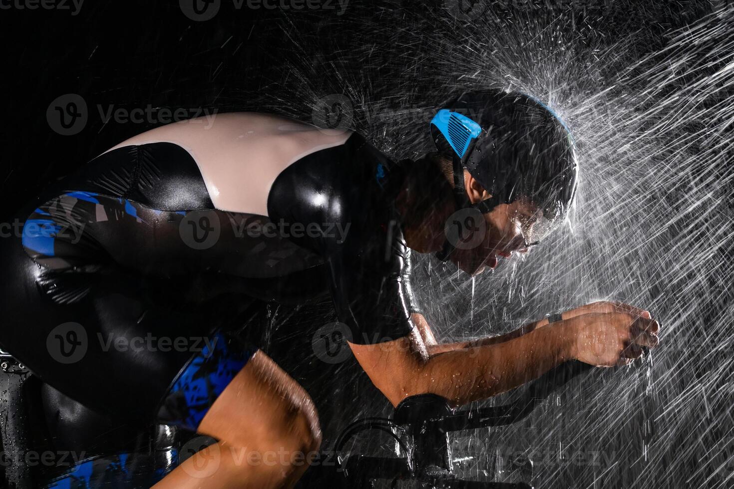 A triathlete braving the rain as he cycles through the night, preparing himself for the upcoming marathon. The blurred raindrops in the foreground and the dark, moody atmosphere in the background add photo