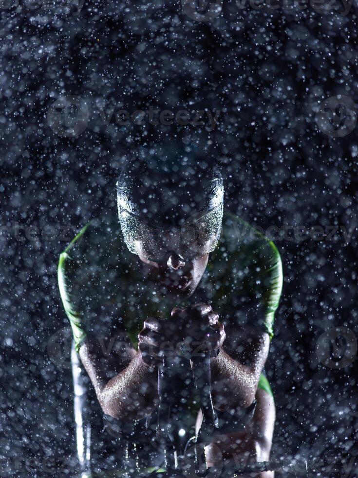 A triathlete braving the rain as he cycles through the night, preparing himself for the upcoming marathon. The blurred raindrops in the foreground and the dark, moody atmosphere in the background add photo