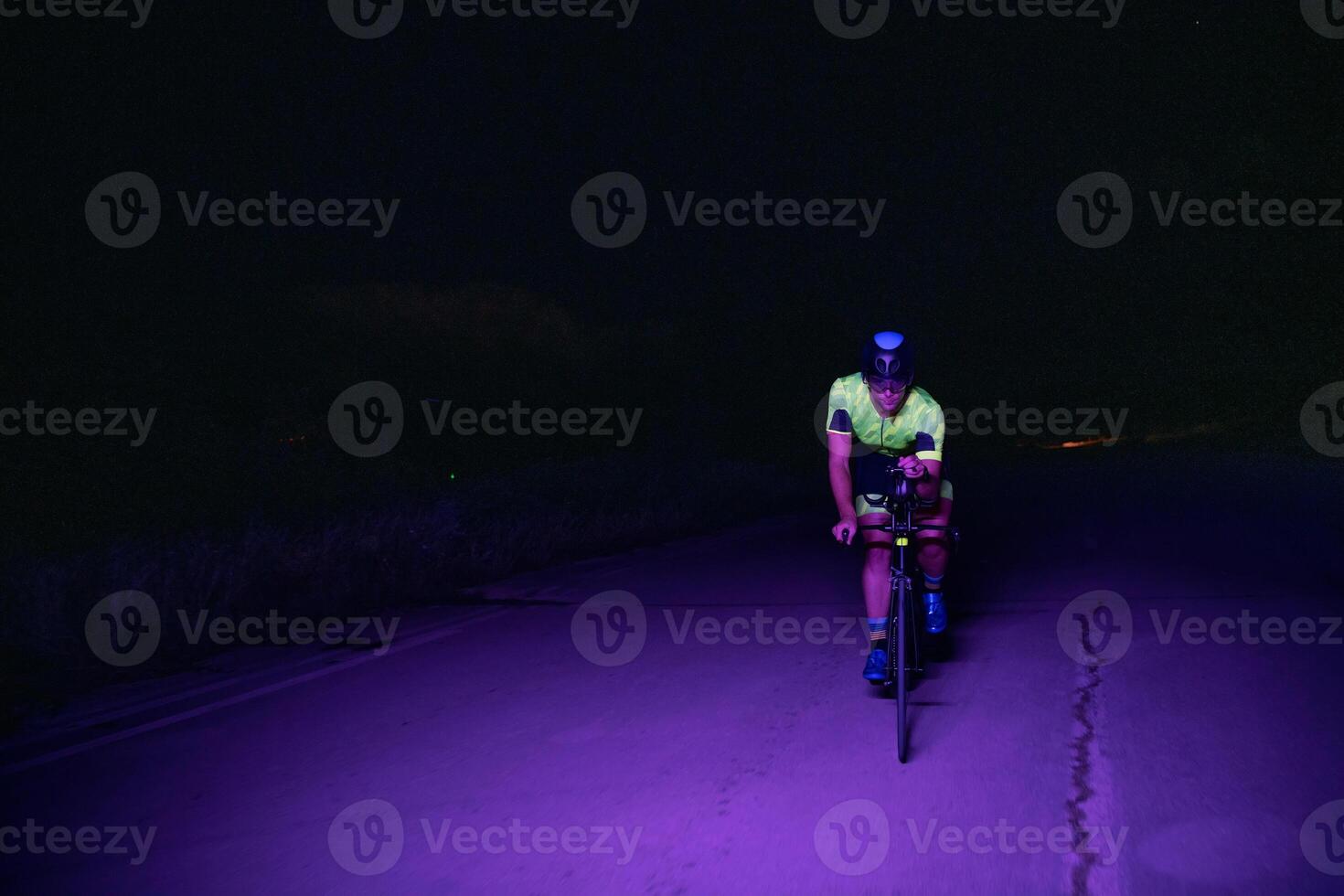 A triathlete rides his bike in the darkness of night, pushing himself to prepare for a marathon. The contrast between the darkness and the light of his bike creates a sense of drama and highlights the photo