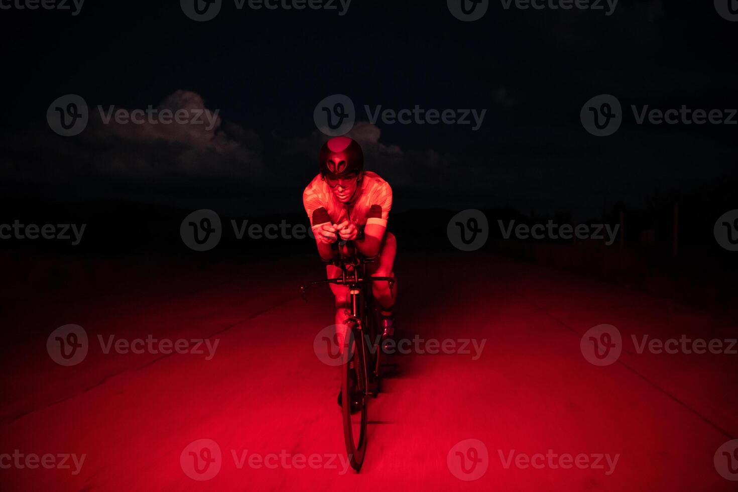A triathlete rides his bike in the darkness of night, pushing himself to prepare for a marathon. The contrast between the darkness and the light of his bike creates a sense of drama and highlights the photo