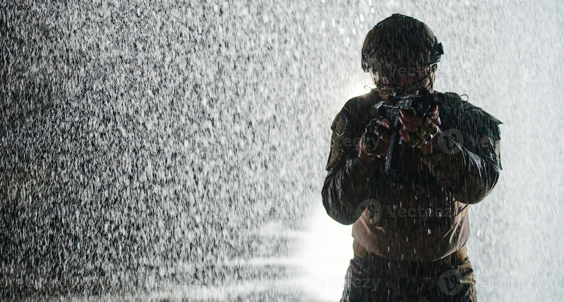 Army soldier in Combat Uniforms with an assault rifle, plate carrier and combat helmet going on a dangerous mission on a rainy night. photo