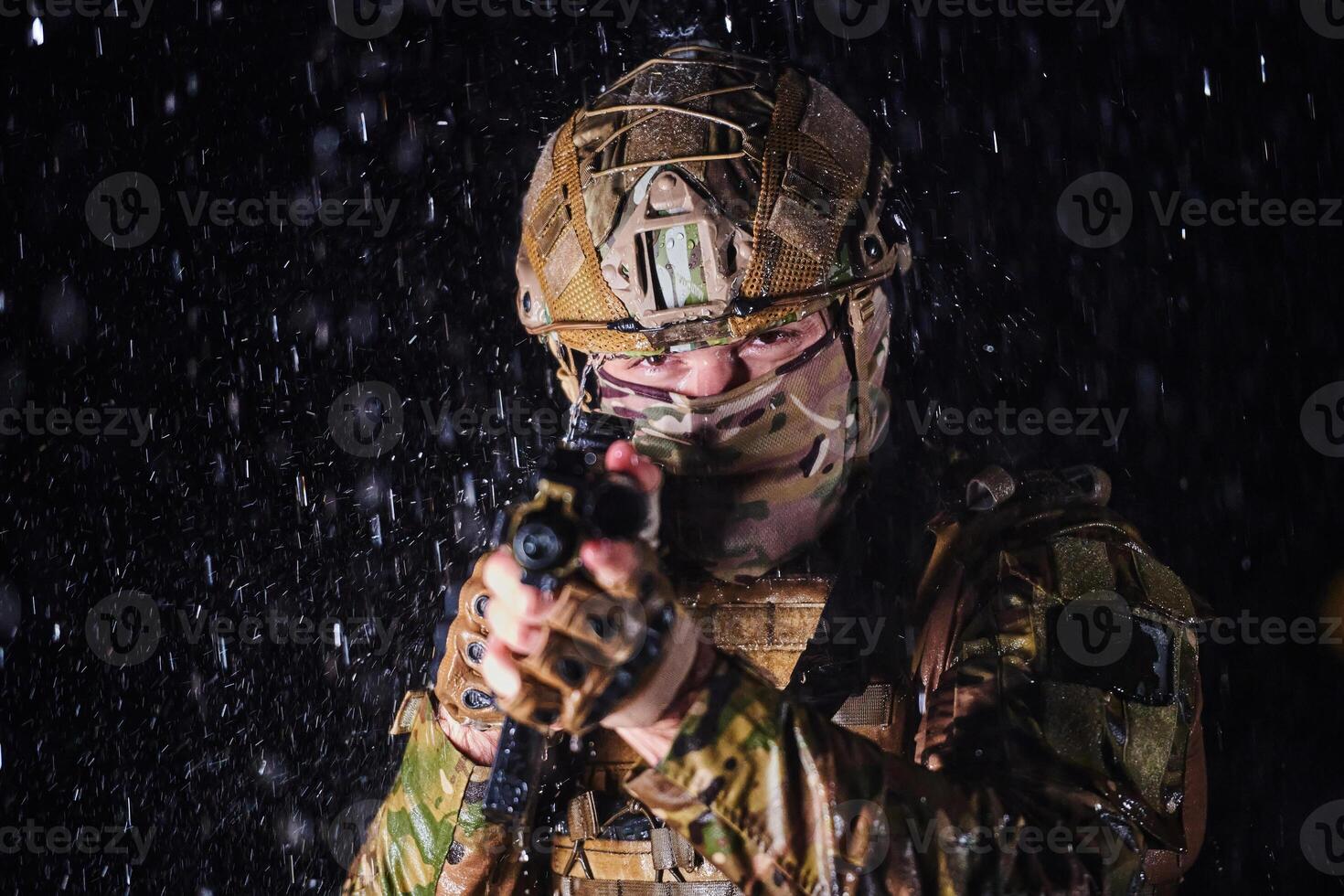 Army soldier in Combat Uniforms with an assault rifle, plate carrier and combat helmet going on a dangerous mission on a rainy night. photo