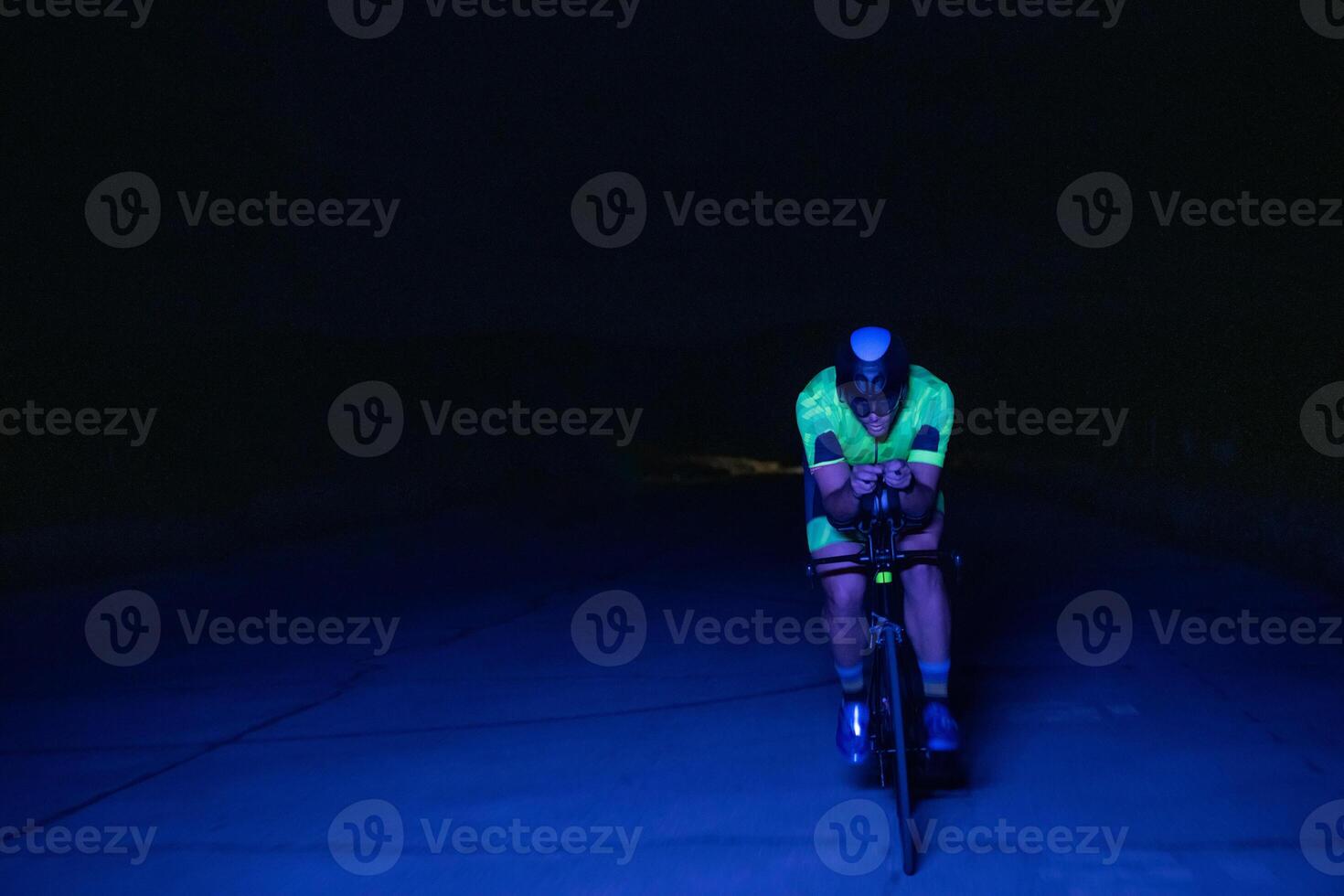 A triathlete rides his bike in the darkness of night, pushing himself to prepare for a marathon. The contrast between the darkness and the light of his bike creates a sense of drama and highlights the photo