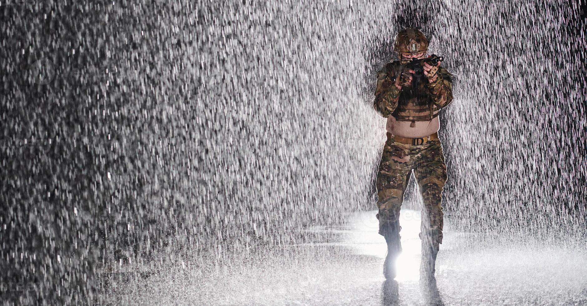 Army soldier in Combat Uniforms with an assault rifle, plate carrier and combat helmet going on a dangerous mission on a rainy night. photo