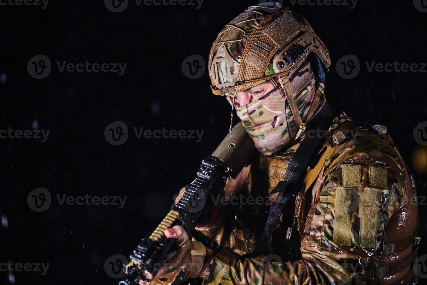 Army soldier in Combat Uniforms with an assault rifle, plate carrier and combat helmet going on a dangerous mission on a rainy night. photo