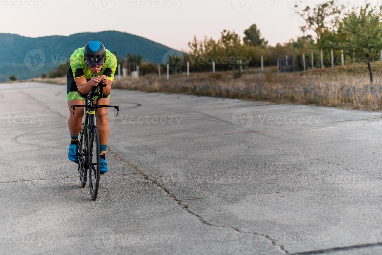 Triathlete riding his bicycle during sunset, preparing for a marathon. The warm colors of the sky provide a beautiful backdrop for his determined and focused effort. photo